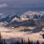 Skier jumping at Kicking Horse Mountain Resort; mountains and trees.